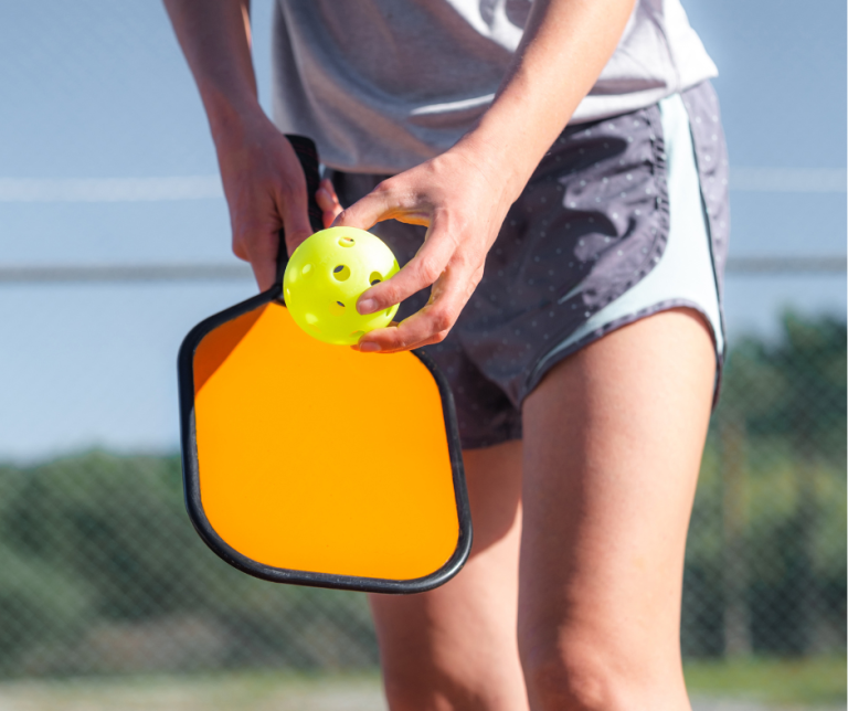 person holding pickleball racquet and ball preparing to serve